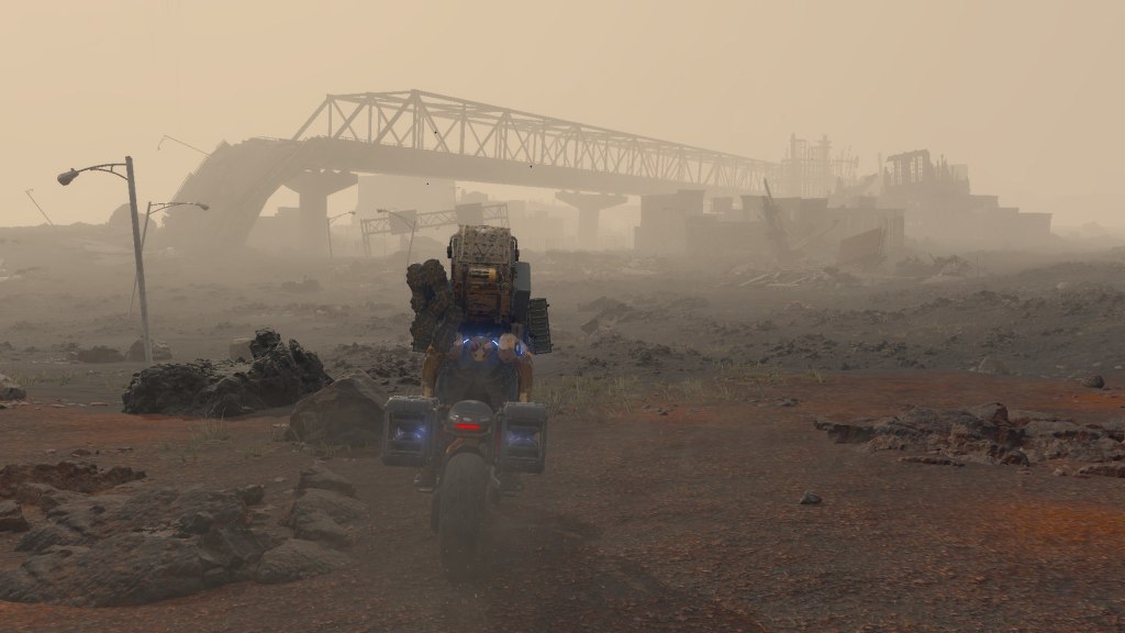 Sam Porter, the main character of Death Stranding, astride a motorbike as he looks at ruins of buildings in the distance.