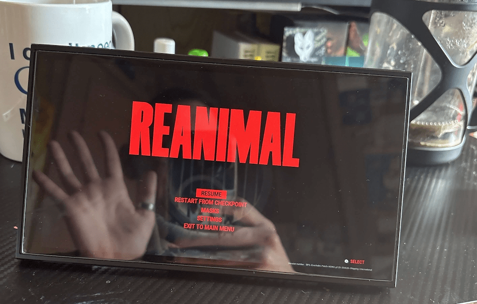 An image depicting a Nintendo Switch 2 propped up showing the game "Reanimal" with the reflection of a hand waving.